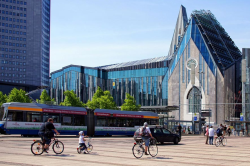 Augustusplatz mit den sehr modernen Bauwerken Paulinum und Aula der Universität.  Vordergrund Bushaltestellen, Straßenbahn, Radfahrer.
